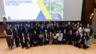 Group photo of BBA students who participated in the Ross Summer Connections program sitting and standing on stage with balloons. 