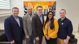 Photo of five Michigan Ross Executive MBA students standing in front a Boston Scientific sign. The team recently completed their ExecMAP project for the company. There are four males and one female student who are all looking at the camera and smiling.
