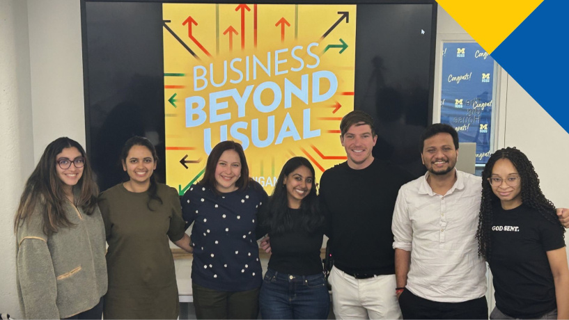 Eight Michigan Ross MBA students in front of the Business Beyond Usual logo